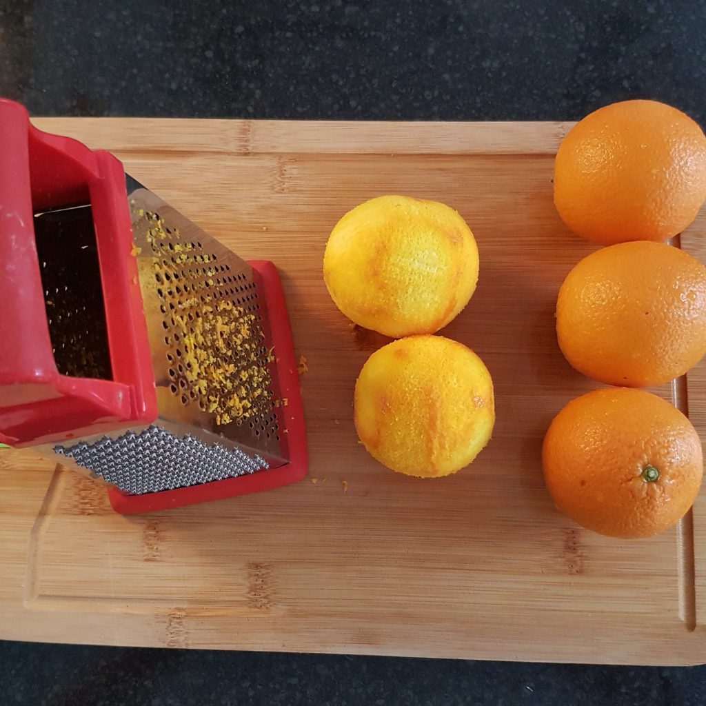 A chopping board with a grater and some oranges